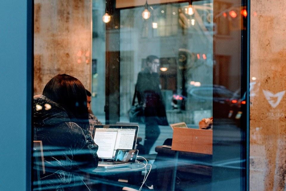 A woman in a cafe, undertaking Digital marketing Surrey on her phone and laptop