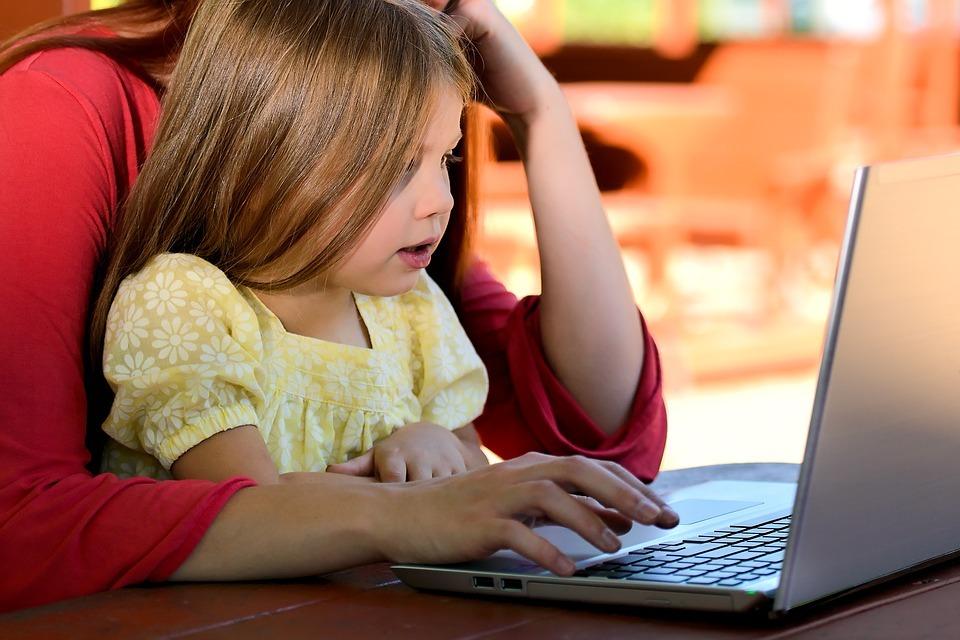 A child sat at a laptop on the lap of an adult | Thunderbolt