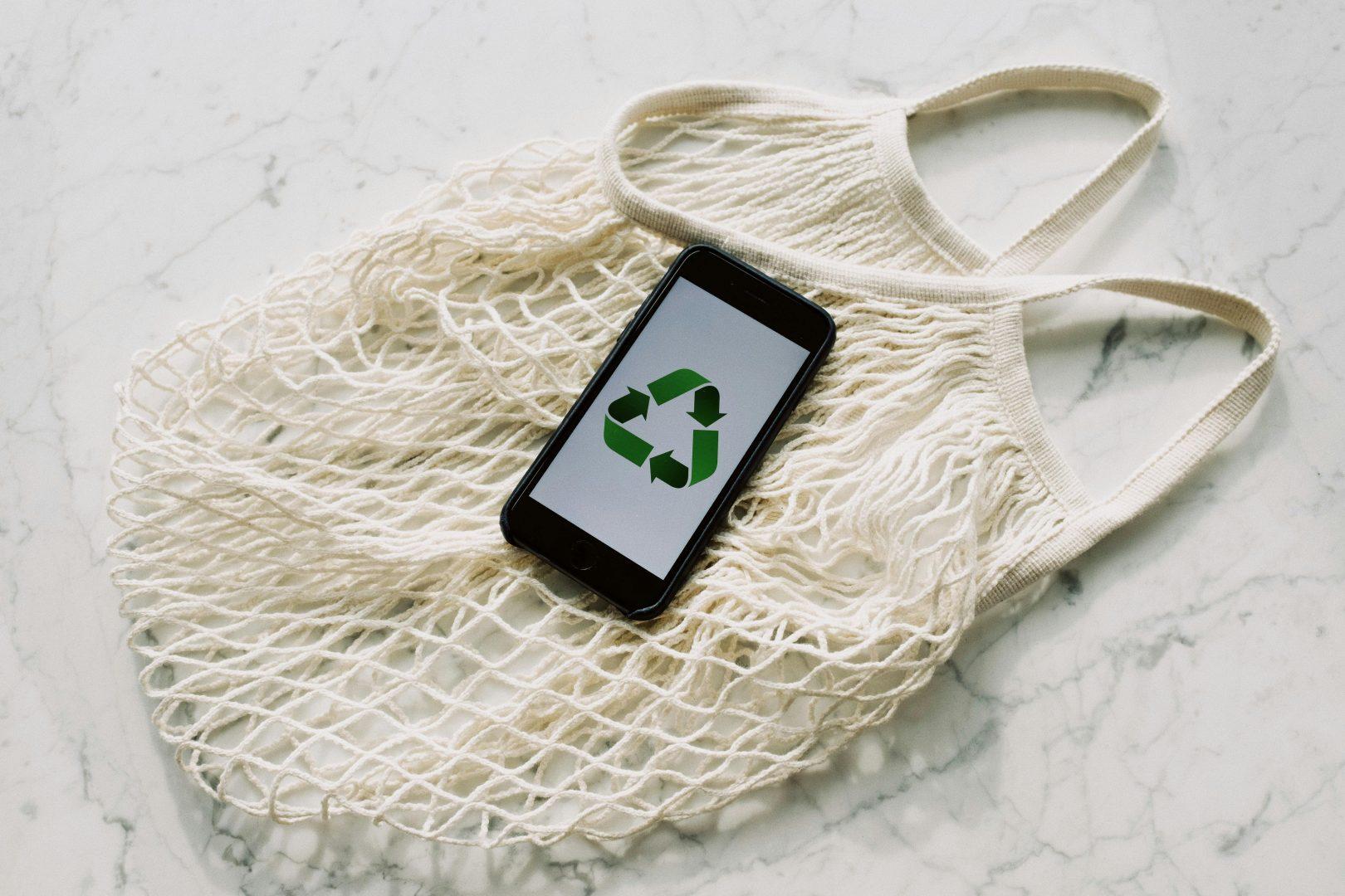 A phone displaying the recycling sign atop a reusable shopping bag | Web Designers in Surrey