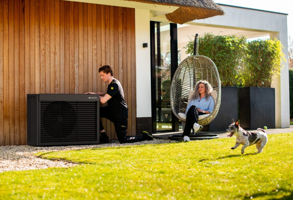 An Adlår heat pump being installed in a garden as the homeowner and a small dog look on