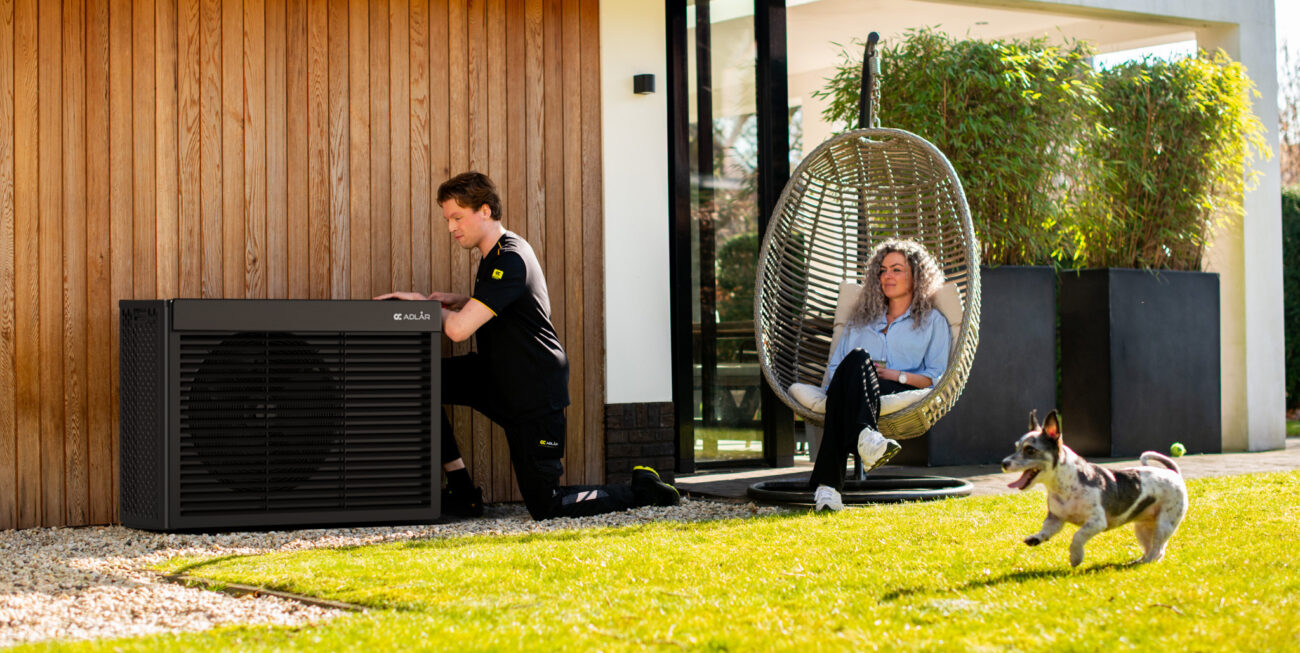 An Adlår heat pump being installed in a garden as the homeowner and a small dog look on