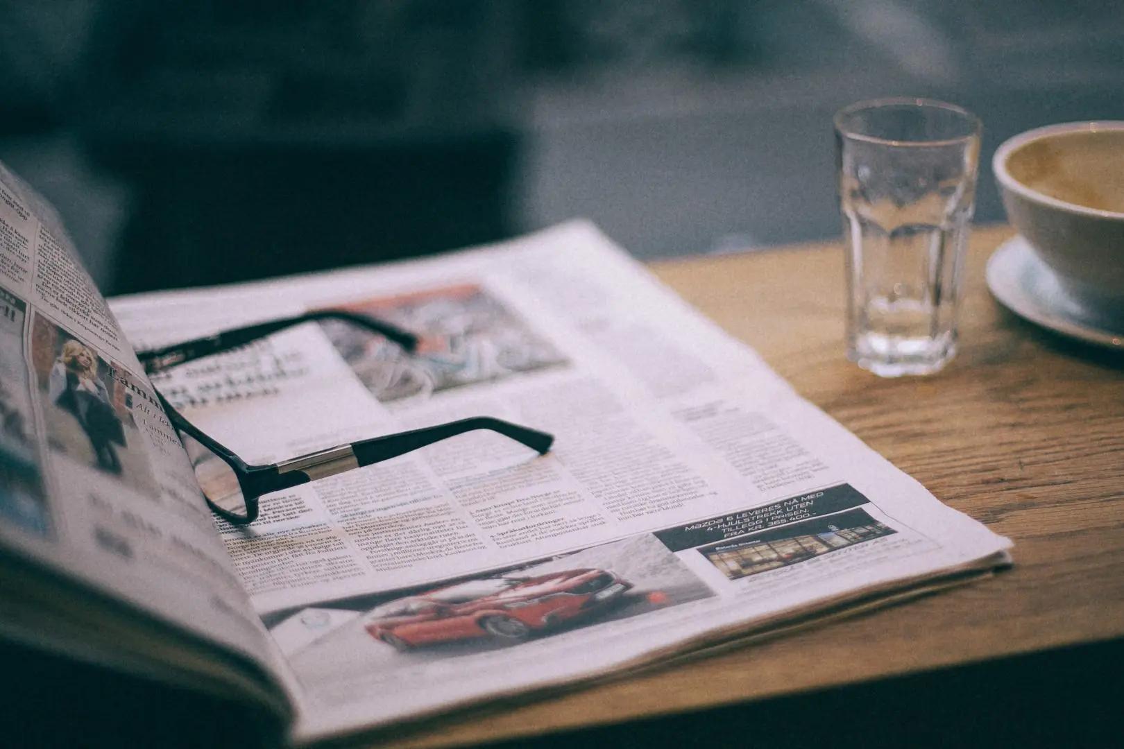 An open newspaper on a table with a pair of glasses on top