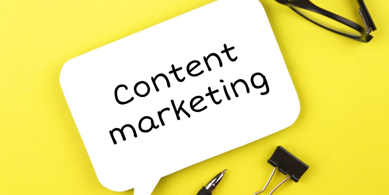 Speech bubble on table top reading "content marketing" with surrounding objects such as glasses, clip, and pen.