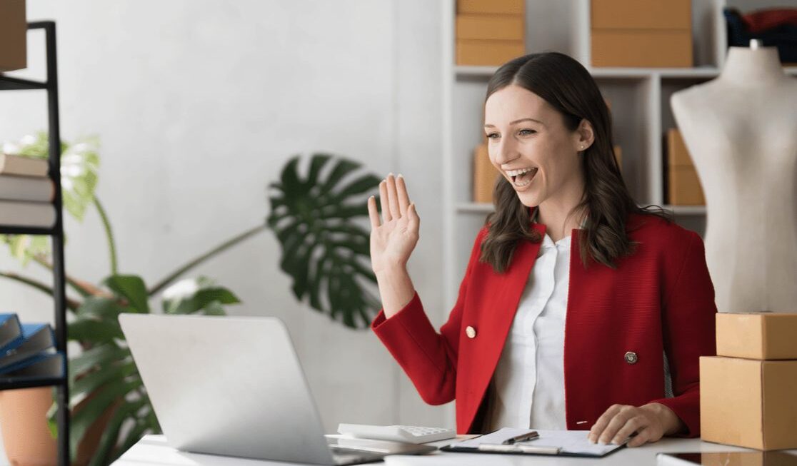 Smartly dressed woman waving to her laptop camera | Social media marketing Surrey