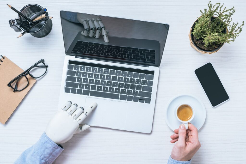 Is AI the future of web design? Robot hand typing on a laptop while human hand holds a cup of tea