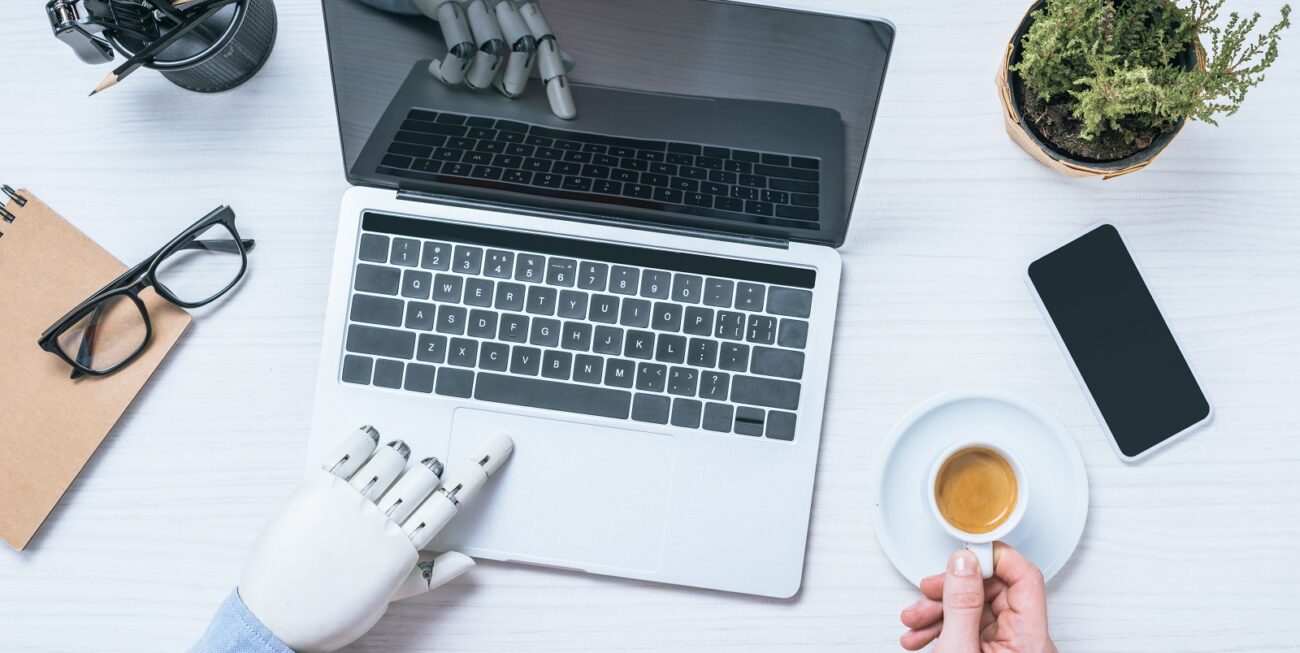Is AI the future of web design? Robot hand typing on a laptop while human hand holds a cup of tea