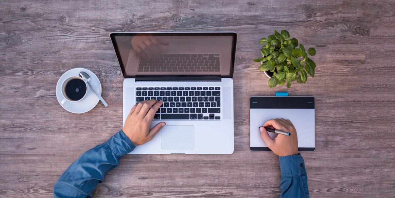 A man working on a laptop next to a cup of coffee and plant