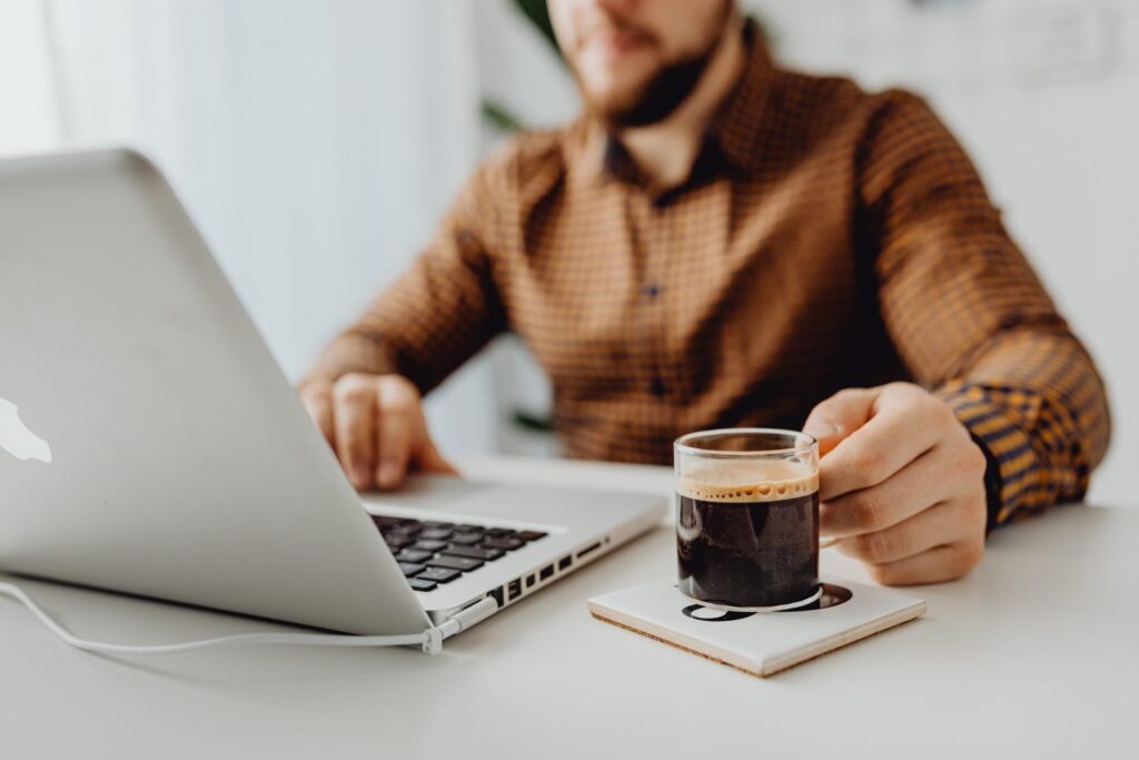 A man holding a mug of coffee and working on his laptop