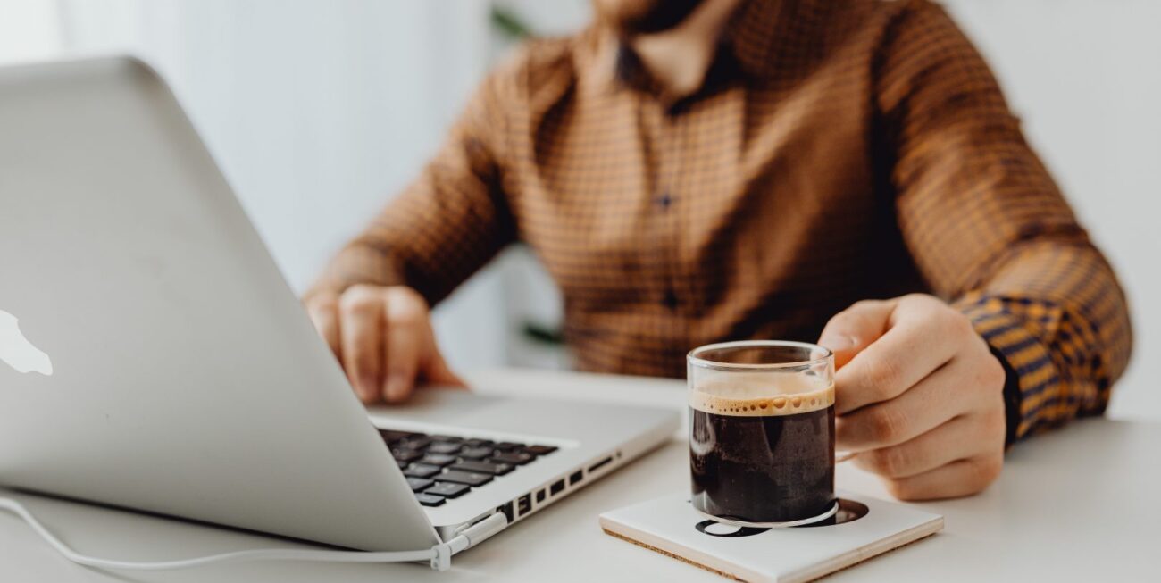 A man holding a mug of coffee and working on his laptop