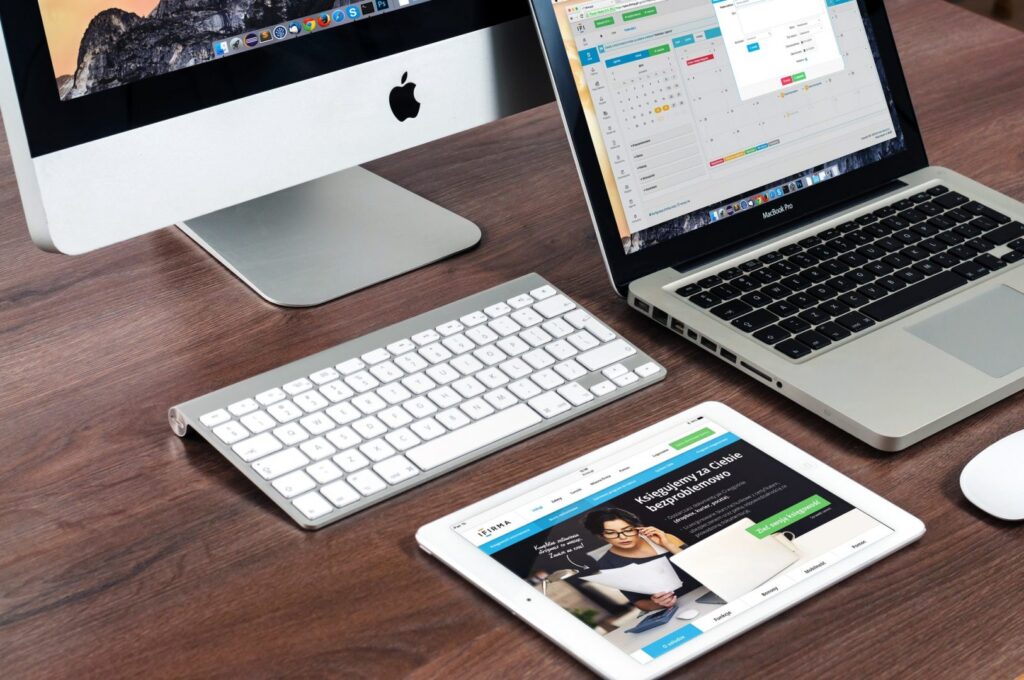 A desk with a desktop monitor, open laptop, and tablet