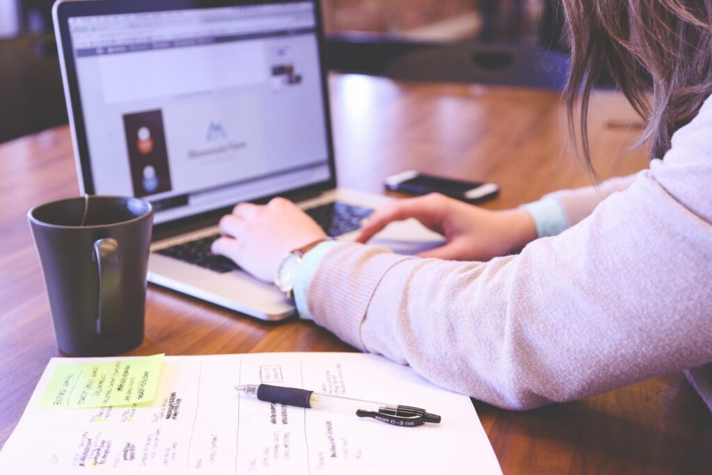 Someone working on a laptop while looking at handwritten notes