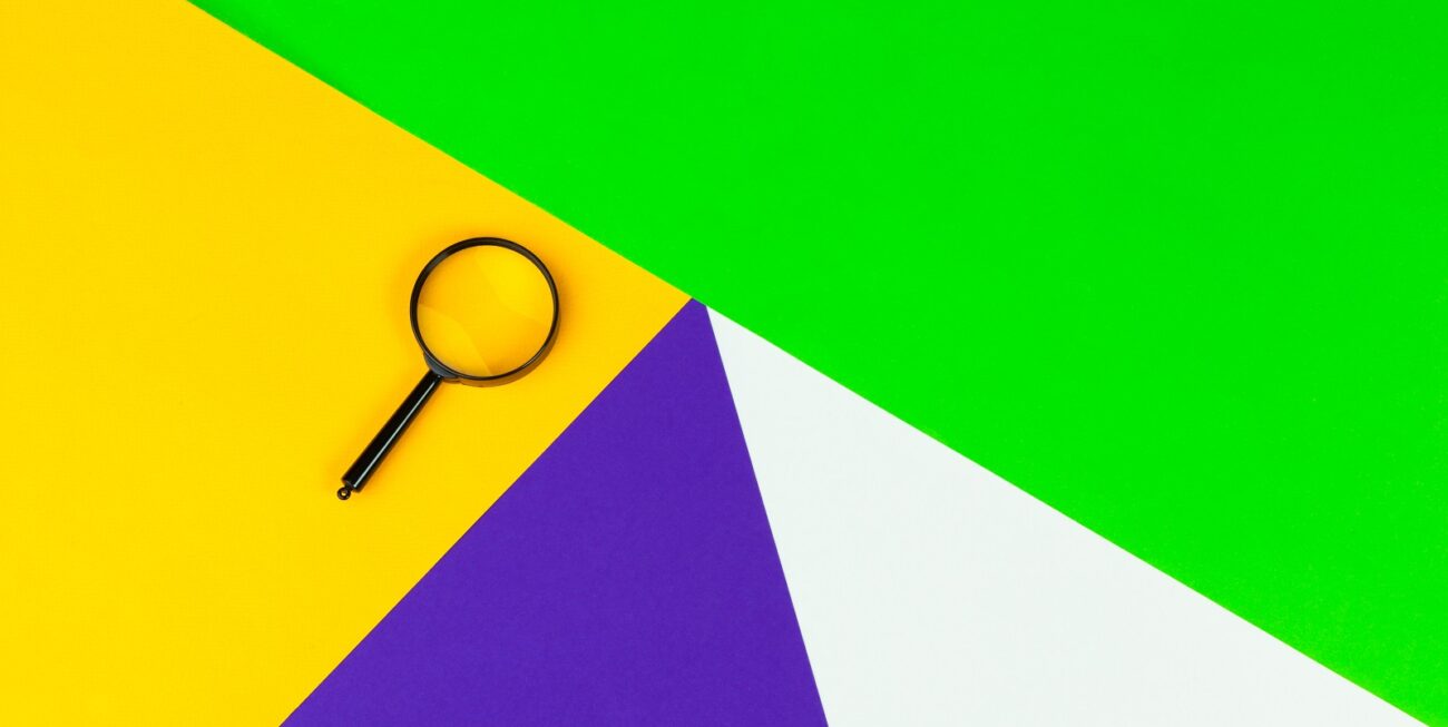 Magnifying glass on colourful geometric paper background, representing keyword research basics