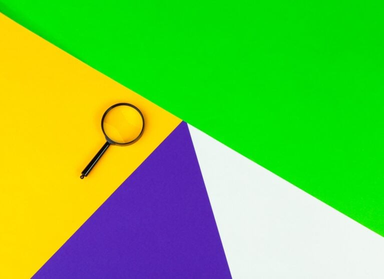 Magnifying glass on colourful geometric paper background, representing keyword research basics
