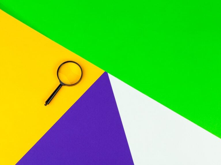 Magnifying glass on colourful geometric paper background, representing keyword research basics