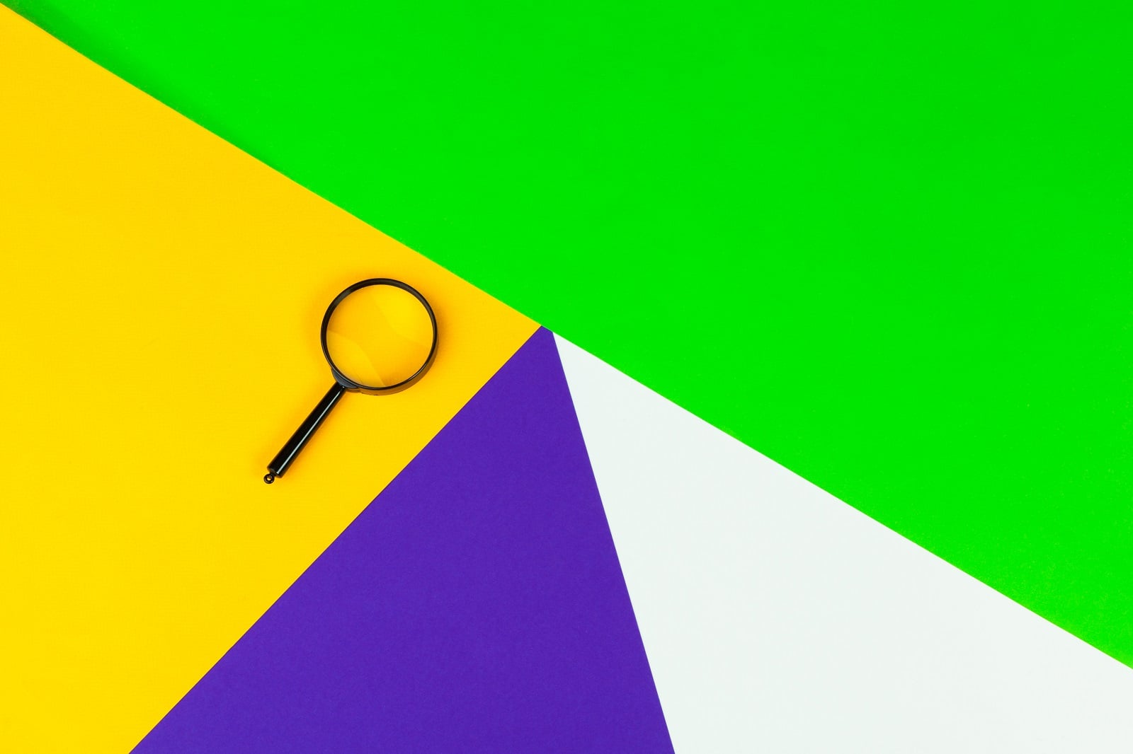 Magnifying glass on colourful geometric paper background, representing keyword research basics