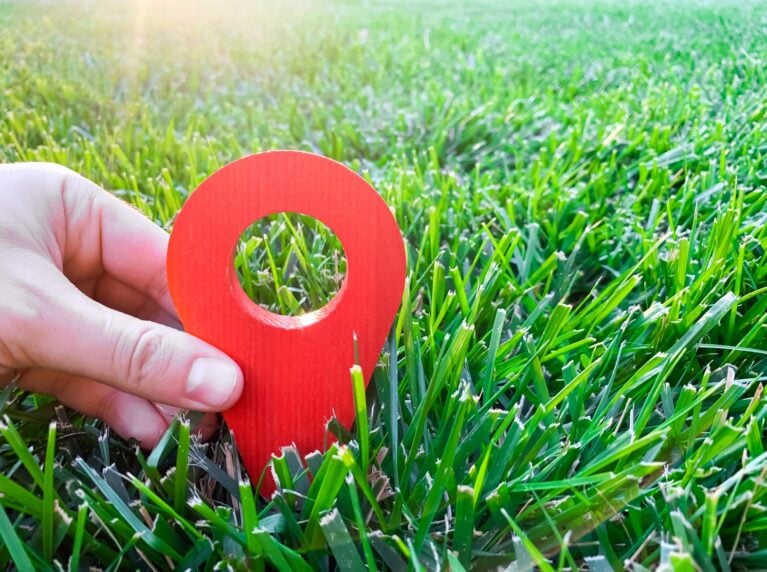 Hand holding a 3D red location pin in green grass, representing local SEO